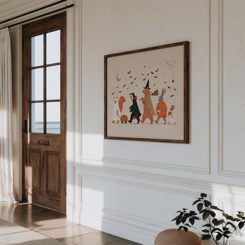 May include: A framed wall art print featuring a whimsical Halloween illustration of a squirrel, badger, bear, rabbit, and mouse dressed in costumes. The animals are walking together under a crescent moon and a swarm of black bats on a beige background.