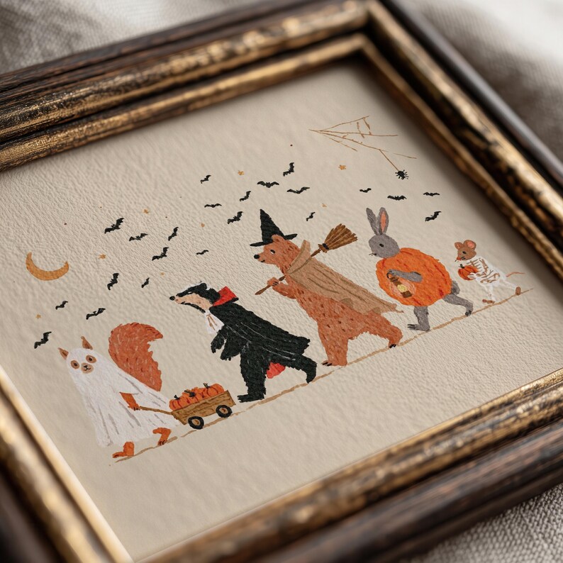 May include: A framed illustration on cream paper featuring a squirrel in a ghost costume pulling a wagon of pumpkins, a badger in a black cape, a bear in a witch hat with a broom, a rabbit in a pumpkin suit, and a mouse in a skeleton costume.