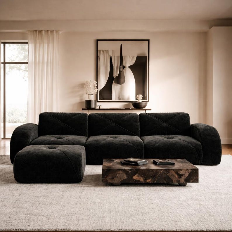 May include: A black modular sofa with a tufted, quilted texture and a matching square ottoman. The sofa features wide, rounded armrests and a low-profile design. A rectangular coffee table with a dark, mottled stone-like finish sits in front.