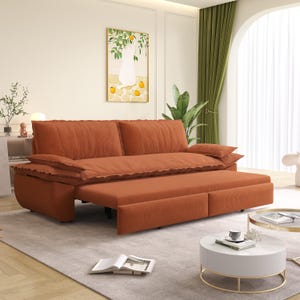 May include: An orange corduroy sofa with a pull-out bed feature. The sofa has two large back cushions and two arm cushions. The pull-out bed is extended, revealing a matching orange corduroy surface. A painting of a cat and lemons hangs on the wall.
