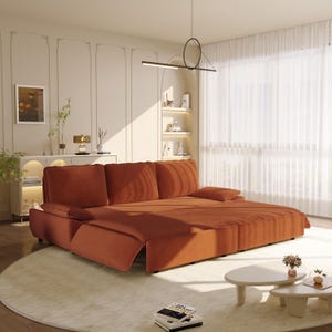 May include: A modern, rust-colored sectional sofa with plush cushions and a chaise lounge. The sofa sits on a light-colored rug in a well-lit living room. The room features a minimalist design with decorative wall panels and a round coffee table.