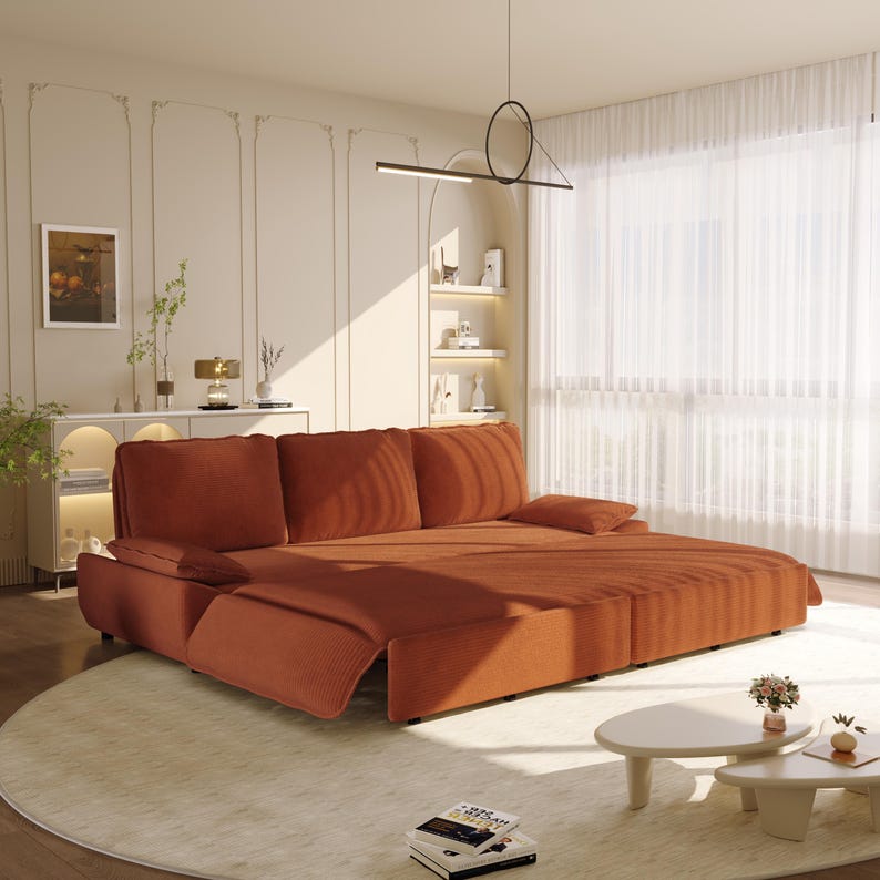 May include: A modern, rust-colored sectional sofa with plush cushions and a chaise lounge. The sofa sits on a light-colored rug in a well-lit living room. The room features a minimalist design with decorative wall panels and a round coffee table.