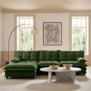 May include: A large, green sectional sofa with tufted cushions. The sofa is in a living room with a marble coffee table, wooden bowls, and a floor lamp. A framed abstract artwork hangs on the wall.