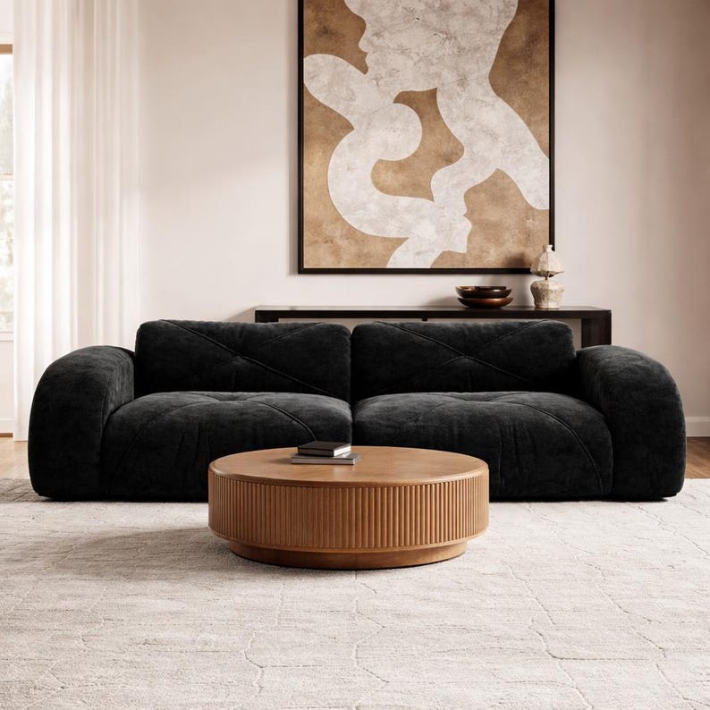 May include: A low-profile black sofa with a tufted, cross-stitched pattern on the cushions and rounded armrests, paired with a round, light brown wooden coffee table featuring a vertically ribbed base and a smooth, flat top surface.