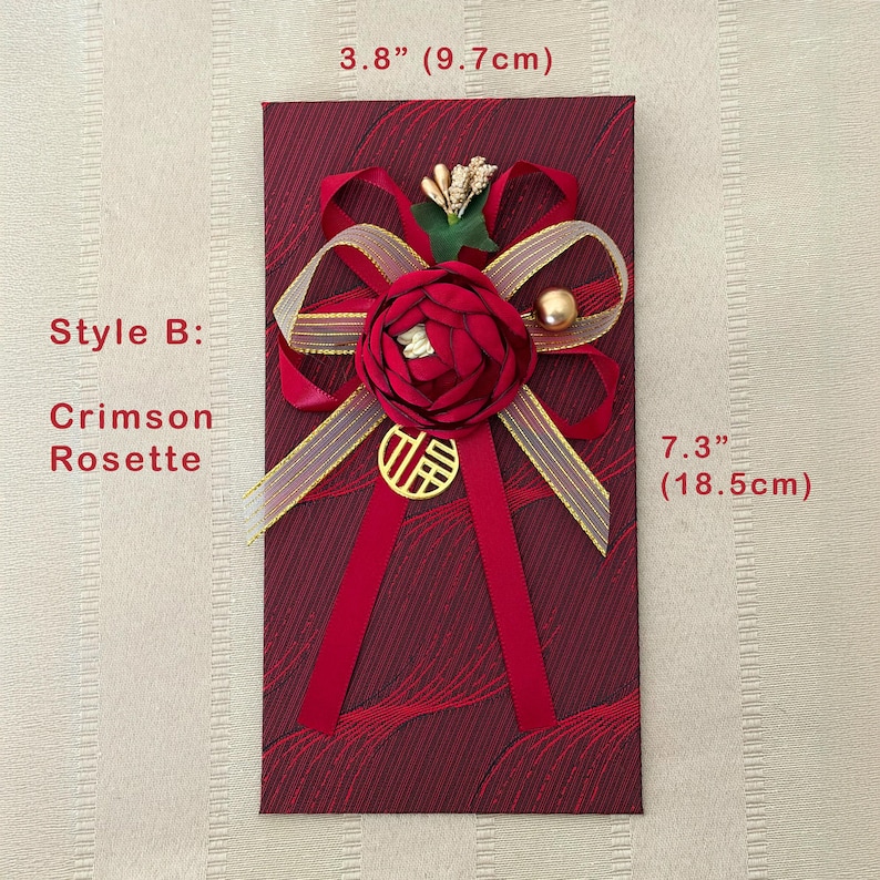 Puede incluir: Sobre rojo carmes&iacute;, de 9,7 cm de ancho y 18,5 cm de alto, con una roseta decorativa y detalles dorados. El sobre presenta una cinta roja, un dije dorado y un adorno floral. El texto "Style B: Crimson Rosette" es visible.