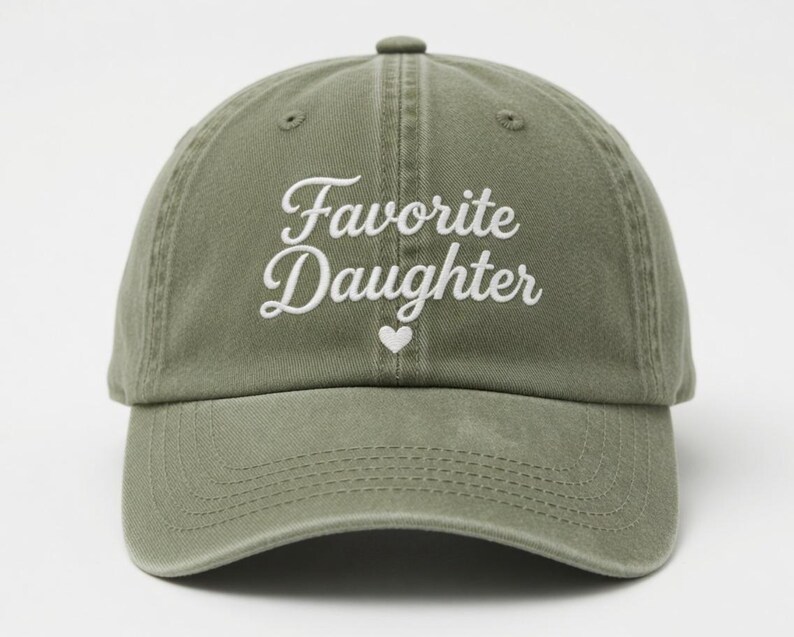 Puede incluir: Gorra de b&eacute;isbol verde oliva con la frase "Favorite Daughter" en escritura blanca, con un peque&ntilde;o coraz&oacute;n blanco. La gorra tiene una visera curva y un cierre de tela.
