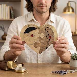Op de afbeelding: Een hartvormige puzzelplaat van acryl en hout met twee in elkaar grijpende stukken met gegraveerde stadsplattegronden van Cleveland en Roma. De namen Erika en Daniel staan bovenaan, samen met de tekst May Love & Friendship Guide Your Journey.