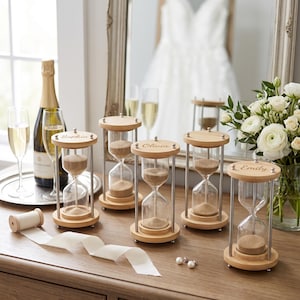 May include: Five wooden hourglasses with clear glass bulbs and tan sand, each featuring a silver metal frame and a light wood base and top. Three of the hourglasses are engraved with the names Sophia, Olivia, and Emily on the top wooden piece.