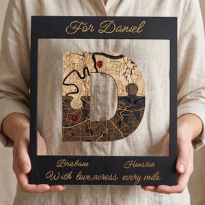 May include: A black wooden frame containing a letter D shaped map collage. The top reads For Daniel. The map features Brisbane and Houston with red heart markers. The bottom text reads Brisbane, Houston, and With love, across every mile.