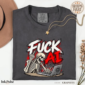 Może przedstawiać: Grafitowy t-shirt z grafiką szkieletu pokazującego środkowy palec podczas pisania na laptopie. Napis FUCK AI wykonany jest biało-czerwonymi literami. Koszulka posiada metkę Comfort Colors oraz złoty naszyjnik z gwiazdką przy dekolcie.