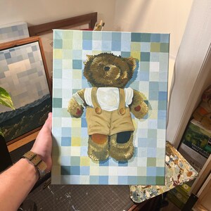 May include: A painting of a brown teddy bear wearing tan overalls and a white shirt, set against a checkered blue and green background. The bear's fur is detailed, and the artwork is on a canvas.