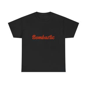 May include: Black t-shirt featuring the word "Bombastic" in red script. The text is slightly curved and is across the chest. A classic crew neck style, suitable for casual wear.