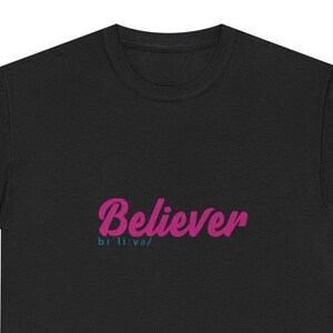 Könnte beinhalten: Ein schwarzes T-Shirt mit Rundhalsausschnitt, auf dem das Wort Believer in einer fetten, magentafarbenen Schreibschrift gedruckt ist. Darunter befindet sich die phonetische Lautschrift biˈliːvə/ in einer kleineren, türkisfarbenen Schrift.