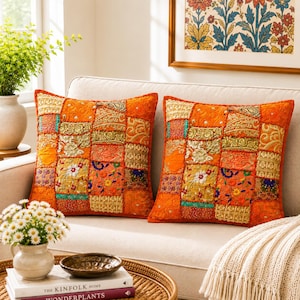May include: Two square throw pillows featuring a vibrant patchwork design in shades of orange, gold, and teal. The fabric panels include intricate embroidery, metallic thread accents, floral patterns, and small reflective mirror embellishments.