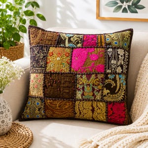 May include: A square decorative pillow featuring a patchwork design of various fabric squares. The pillow displays intricate embroidery, beadwork, and metallic thread accents in vibrant colors including hot pink, gold, brown, and blue.