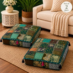Può includere: Un set di due cuscini da pavimento quadrati caratterizzati da un design patchwork di vari quadrati di tessuto verde, verde acqua e oro con intricati motivi floreali e di uccelli. Ogni cuscino presenta bordini verde scuro e nappe angolari.