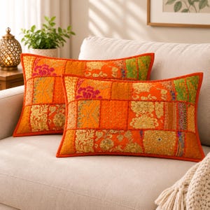 May include: Two rectangular throw pillows featuring a vibrant orange patchwork design. Each pillow is composed of various fabric panels in shades of orange, gold, and green, decorated with intricate gold embroidery, sequins, and floral patterns.