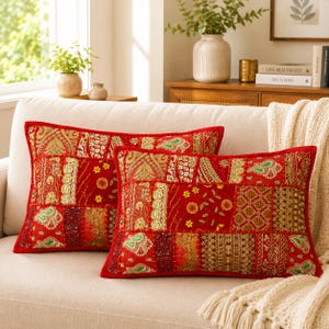 May include: Two rectangular throw pillows featuring a vibrant red patchwork design with intricate gold embroidery, metallic thread accents, and small green floral motifs. The fabric displays a variety of textured patterns and decorative stitching.