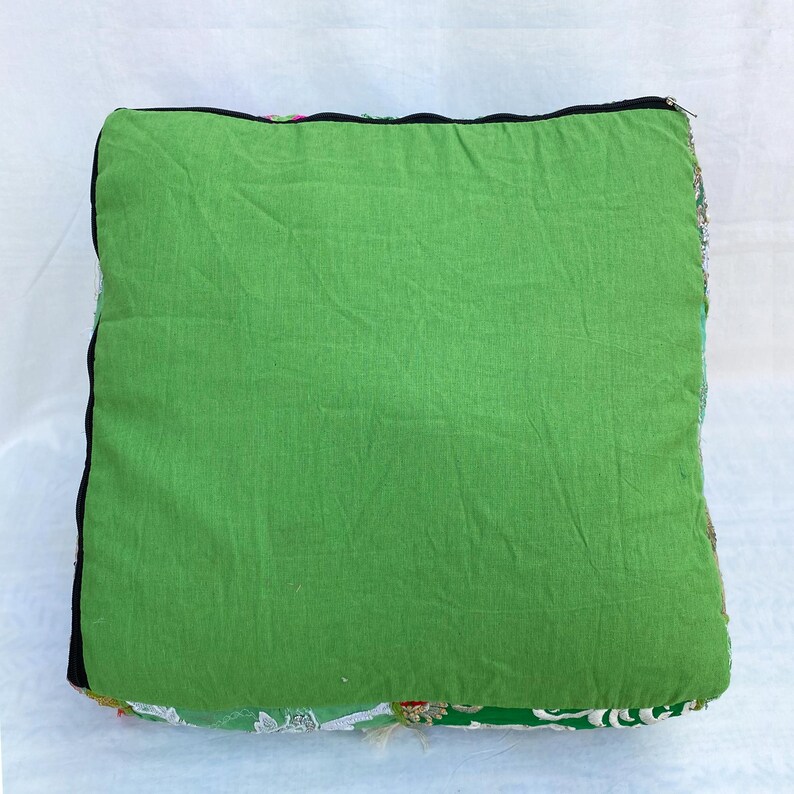 K&ouml;nnte beinhalten: Quadratisches gr&uuml;nes Kissen mit schwarzem Rand. Das Kissen hat eine einfarbige gr&uuml;ne Oberseite und eine gemusterte Unterseite mit floralen und Pailletten-Details. Das Kissen befindet sich auf wei&szlig;em Hintergrund.