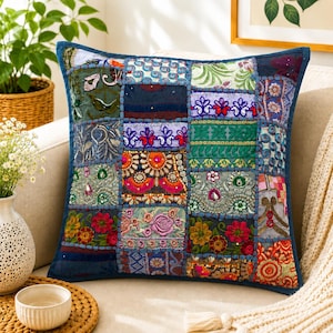 May include: A square throw pillow featuring a patchwork design of various fabric squares. The fabric includes diverse patterns, floral embroidery, sequins, and beadwork in vibrant colors like red, green, blue, orange, and purple, all bordered by blue piping.