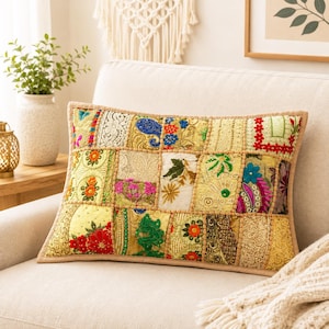 May include: A rectangular throw pillow featuring a patchwork design of various fabrics in shades of gold, yellow, green, and red. The surface is decorated with intricate embroidery, floral patterns, sequins, and lace textures, finished with a tan border.