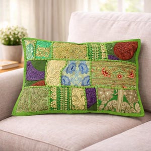 Könnte beinhalten: Rechteckiges Zierkissen mit Patchwork-Design. Das Kissen hat verschiedene grüne Stoffquadrate mit gestickten Mustern und einen hellgrünen Rand. Das Kissen liegt auf einem hellen Sofa.