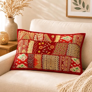 May include: A rectangular throw pillow featuring a vibrant red base with a patchwork design. The surface is adorned with various gold, green, and yellow embroidered fabric panels, intricate metallic thread detailing, and small floral bead accents.