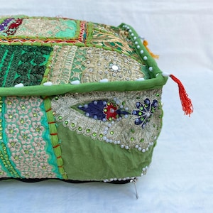 K&ouml;nnte beinhalten: Ein quadratisches, dekoratives Bodenkissen mit Patchwork-Design. Das Kissen hat verschiedene Gr&uuml;nt&ouml;ne, Gold- und Cremestoffe, verziert mit Stickereien, Pailletten und Perlen. Ein gr&uuml;ner Rand und eine rote Quaste verleihen diesem einzigartigen Wohnaccessoire den letzten Schliff.