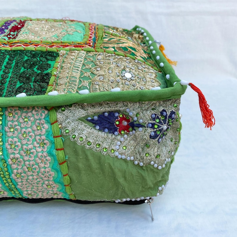 K&ouml;nnte beinhalten: Ein quadratisches, dekoratives Bodenkissen mit Patchwork-Design. Das Kissen hat verschiedene Gr&uuml;nt&ouml;ne, Gold- und Cremestoffe, verziert mit Stickereien, Pailletten und Perlen. Ein gr&uuml;ner Rand und eine rote Quaste verleihen diesem einzigartigen Wohnaccessoire den letzten Schliff.