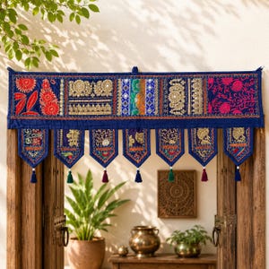 May include: A rectangular blue fabric valance featuring intricate embroidery, gold-toned metallic thread work, and small reflective mirror accents. The bottom edge has seven pointed, embroidered panels, each finished with a small hanging tassel.