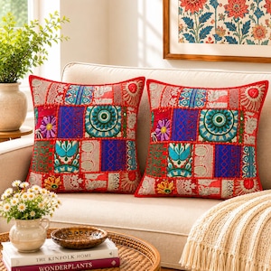 May include: Two square throw pillows featuring a vibrant patchwork design with red, blue, and green fabric panels. The pillows display intricate embroidered floral motifs, circular patterns, and geometric shapes with decorative stitching throughout.