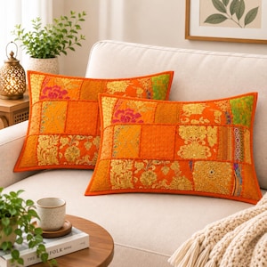 May include: Two rectangular throw pillows featuring a vibrant orange patchwork design. Each pillow is composed of various fabric squares with intricate gold embroidery, floral patterns, and textured stitching, finished with a solid orange border.
