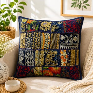 May include: A square throw cushion featuring a patchwork design of dark blue fabric panels. Each panel is decorated with intricate embroidery in gold, red, orange, and green thread, showcasing floral patterns, geometric shapes, and metallic accents.