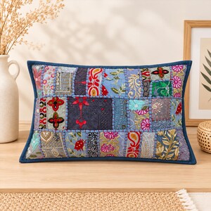 May include: A rectangular throw pillow featuring a patchwork design of various embroidered fabrics in shades of blue, red, pink, and gold. The pillow is finished with a dark blue border and visible stitching between the fabric panels.