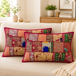 May include: Two rectangular throw pillows featuring a vibrant patchwork design. The fabric consists of various squares in shades of magenta, gold, green, and blue, decorated with intricate metallic embroidery, sequins, and diverse floral patterns.