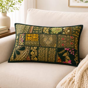 May include: A rectangular throw pillow featuring a dark green base with a patchwork design of various embroidered fabric panels. The panels display intricate gold, yellow, pink, and green floral and geometric patterns with detailed stitching.
