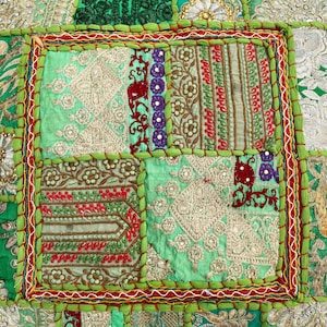 K&ouml;nnte beinhalten: Nahaufnahme eines Patchwork-Textils mit einer Vielzahl von Mustern und Farben. Das Design zeigt Quadrate aus gr&uuml;nen, roten, lila und goldenen Stoffen. Die R&auml;nder sind mit gr&uuml;nen und roten N&auml;hten versehen, wodurch eine dekorative Bord&uuml;re entsteht.