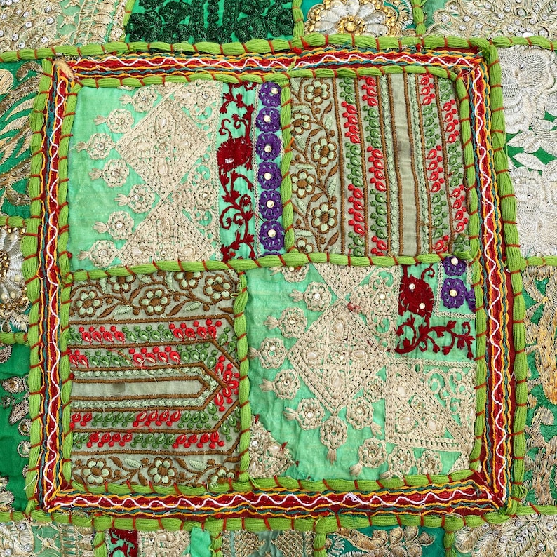 K&ouml;nnte beinhalten: Nahaufnahme eines Patchwork-Textils mit einer Vielzahl von Mustern und Farben. Das Design zeigt Quadrate aus gr&uuml;nen, roten, lila und goldenen Stoffen. Die R&auml;nder sind mit gr&uuml;nen und roten N&auml;hten versehen, wodurch eine dekorative Bord&uuml;re entsteht.