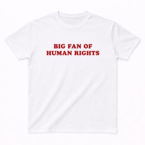 Könnte beinhalten: Ein weißes kurzärmeliges T-Shirt mit dem Text BIG FAN OF HUMAN RIGHTS, der in fetten roten Großbuchstaben mittig auf der Brust aufgedruckt ist. Das Kleidungsstück hat einen Rundhalsausschnitt und eine Standardpassform aus weißem Stoff.