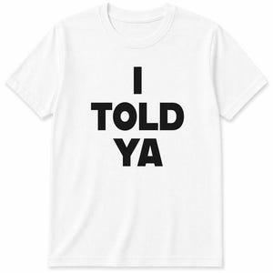 Op de afbeelding: Een wit t-shirt met korte mouwen en de tekst I TOLD YA in dikke zwarte hoofdletters in het midden op de borst. Het kledingstuk heeft een klassieke ronde hals en een rechte zoom, wat zorgt voor een strakke en eenvoudige uitstraling.