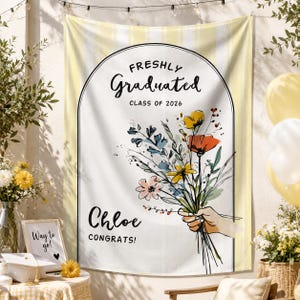 May include: A graduation tapestry featuring a floral bouquet illustration. The text reads "Freshly Graduated Class of 2026" and "Chloe Congrats!". The background is white with yellow stripes.