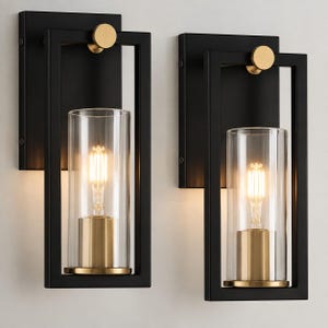 May include: A pair of wall sconces featuring a rectangular black metal frame, a cylindrical clear glass shade, and a brass-toned socket. Each fixture includes a round brass accent at the top and an exposed filament light bulb inside the glass.
