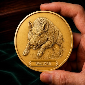 May include: A circular gold-colored coin featuring a detailed relief of a wild boar in a charging stance. Below the boar, a rectangular plaque is embossed with the text WALKER in capital letters. The coin has a smooth, raised outer rim.