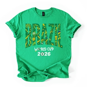 May include: A green t-shirt with the word "BRAZIL" in large, yellow, and green letters. The word is filled with various patterns and symbols. Below the word is "WORLD CUP 2026" with soccer ball graphics.