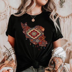 May include: Black t-shirt featuring a colorful, patterned design in the shape of a country. The design incorporates a variety of geometric shapes and colors, including red, blue, and orange. The shirt has short sleeves and a crew neck.
