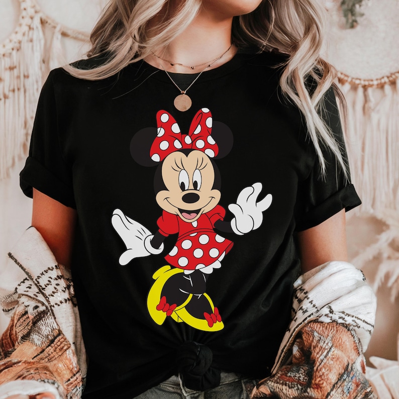 May include: Black t-shirt featuring a Minnie Mouse graphic. Minnie is depicted in a red dress with white polka dots, a matching bow, and yellow shoes. The design is a classic cartoon style.