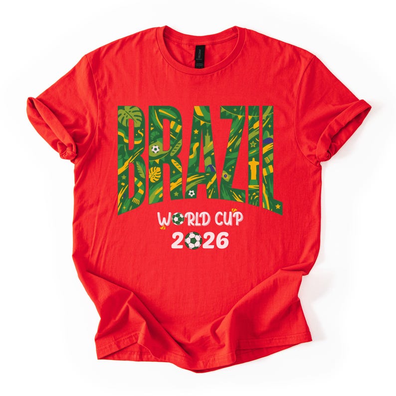 May include: Red t-shirt with the word "BRAZIL" in green and yellow, filled with tropical patterns. Below, "WORLD CUP 2026" is printed in white, with soccer ball graphics. The shirt is a casual wear item.