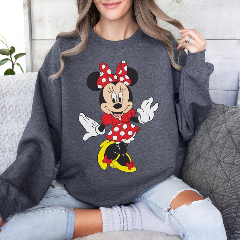 Op de afbeelding: Donkergrijze sweatshirt met een Minnie Mouse-ontwerp. Het stripfiguur is afgebeeld in een rode jurk met witte stippen, een bijpassende strik en gele schoenen. De sweatshirt heeft lange mouwen en een ronde hals.