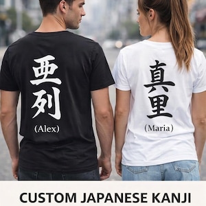 以下が含まれることがあります： 背中に日本語の漢字がプリントされた黒と白のTシャツ。黒いシャツには「Alex」、白いシャツには「Maria」という名前が英語で漢字の下に書かれています。画像には「CUSTOM JAPANESE KANJI NAME T-SHIRT」というテキストも含まれています。
