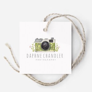 May include: A white tag with a green and white camera illustration with green leaves and red flowers. The text "Daphne Chandler Photography" is below the camera.